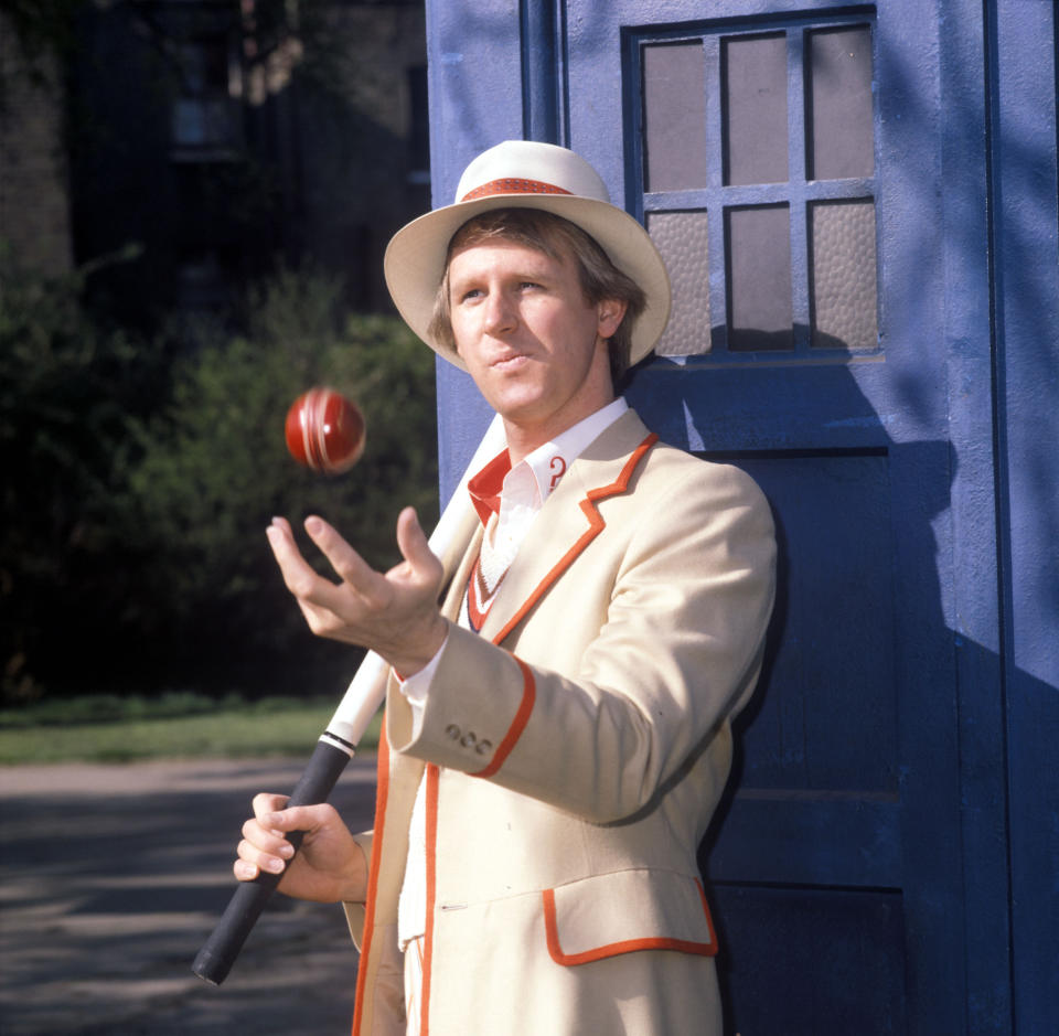 Peter Davison's The Doctor, wearing his cream costume and hat, while holding a cricket bat and ball stood in front of the TARDIS. (Avalon/Getty Images)