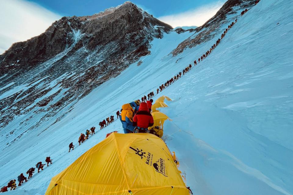 A long line of mountaineers making their way up a steep snow-covered slop on Mount Everest.
