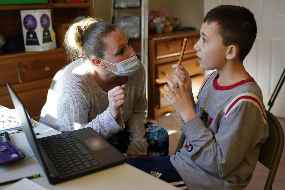 Paraprofessional Jessica Wein helps Josh Nazzaro with his classwork while attending class virtually from his home in Wharton, N.J., Wednesday, Nov. 18, 2020. Without any in-school special education services for months, Nazzaro’s normally sweet demeanor has sometimes given way to aggressive meltdowns that had been under control before the pandemic. The teenager, who has autism and is nonverbal, often wanted no part of his online group speech therapy sessions, and when he did participate, he needed constant hands-on guidance from aides hired by his family. (AP Photo/Seth Wenig)