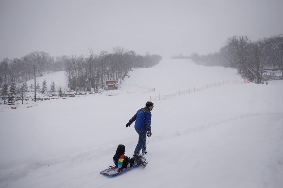 A man pulls a child in a sled by the shut-down slopes of Blue Mountain Ski Resort in The Blue Mountains, Ontario, on the first day of a provincial lockdown amid a 12-day trend of over 2,000 daily COVID-19 cases, Saturday, Dec. 26, 2020. (Cole Burston/The Canadian Press via AP)