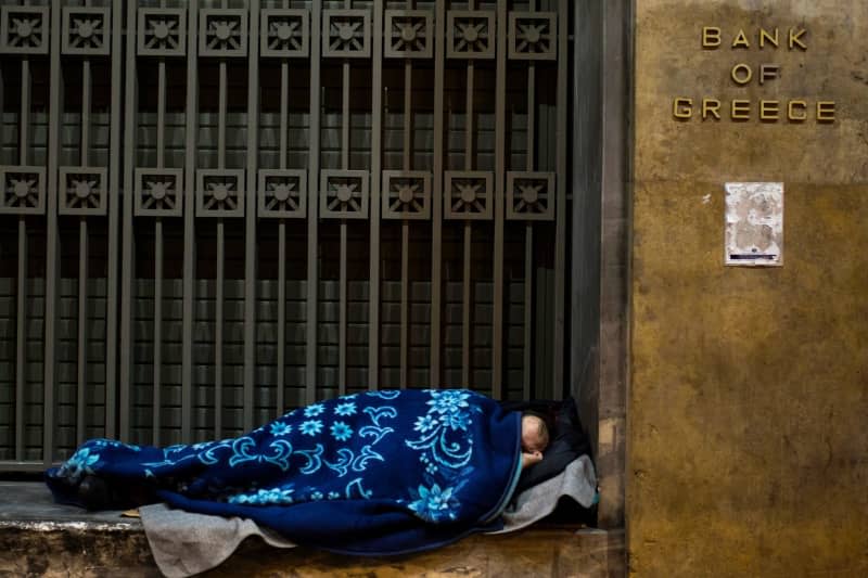 A homeless person sleeps outside the entrance of bank of Greece. In protest against the rising cost of living and comparatively low wages, Greek journalists went on strike for 24 hours on Tuesday. picture alliance / Angelos Tzortzinis/dpa