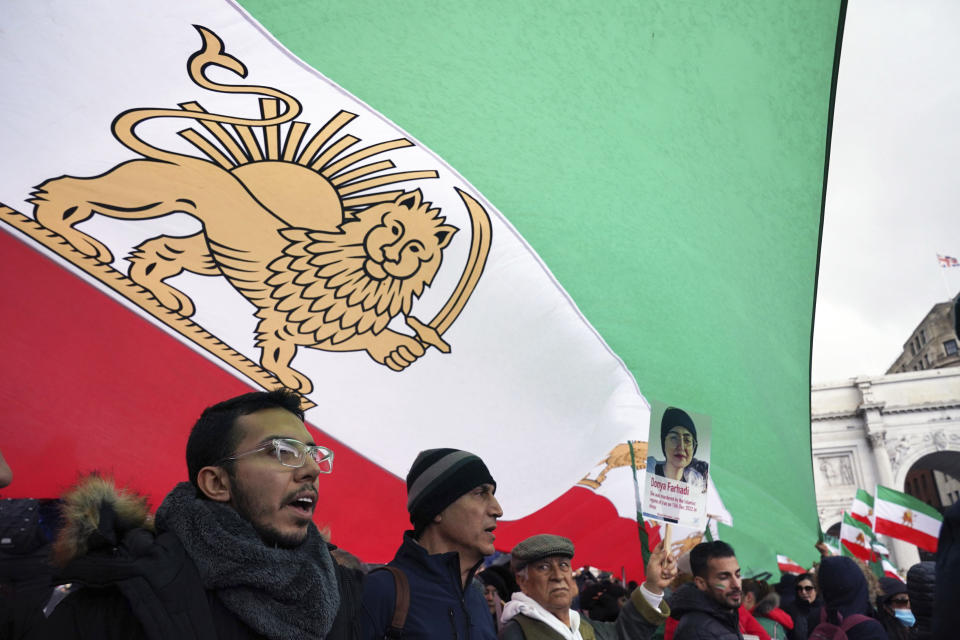 Protesters shelter under a pre-revolutionary flag as they gather at Marble Arch before they march to Trafalgar Square to protest against the Islamic Republic in Iran following the death of Mahsa Amini, in London, Sunday, Jan. 8, 2023. (Jonathan Brady/PA via AP)