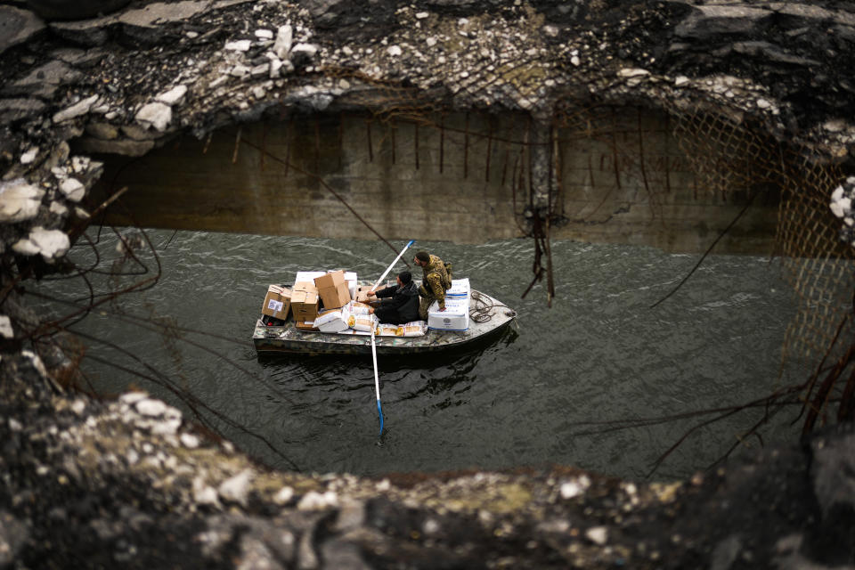 Yuri Shapovalov rows a boat full of goods and with a Ukrainian serviceman they cross the Siverskyi-Donets river under a destroyed bridge in Staryi-Saltiv, Ukraine, Wednesday, Oct. 5, 2022. Shapovalov helps locals daily to cross the river with goods as the bridge was mostly destroyed during fighting. (AP Photo/Francisco Seco)