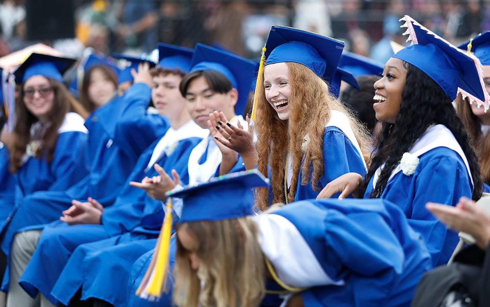 Students laugh as one of them discovers a $100 bill left under her seat by school committee Vice Chairman Frank Santoro during Quincy High School's commencement ceremonies at Veterans Stadium on Monday, June 5, 2023.