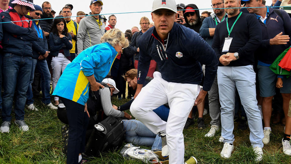 Brooks Koepka (R) checks on the injured spectator. (Photo by FRANCK FIFE / AFP)