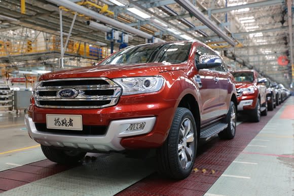 A line of Ford Everest SUVs at the end of a factory production line. The first Everest in line has a Chinese-language license plate.