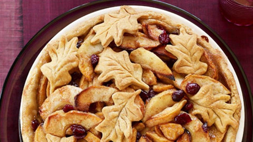 fall apple cranberry pie in a white pie dish with pie crust leaves on top