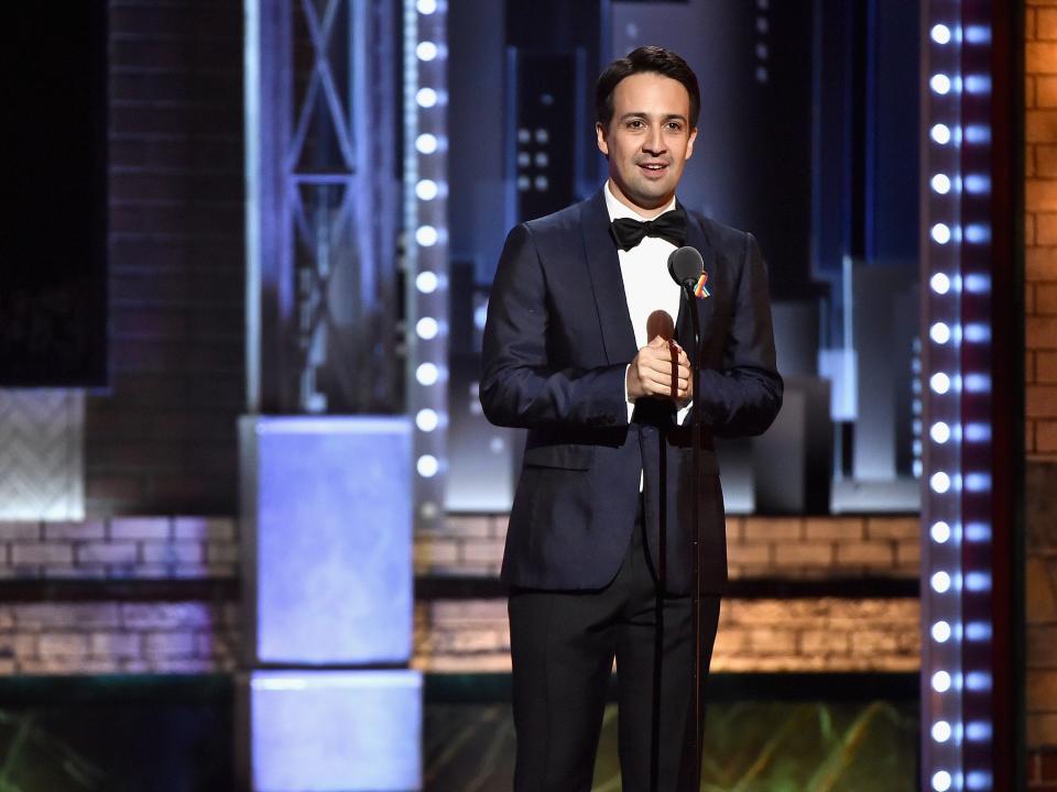 Lin-Manuel Miranda dressed in a tuxedo speaking into a microphone at the 2017 Tony Awards.