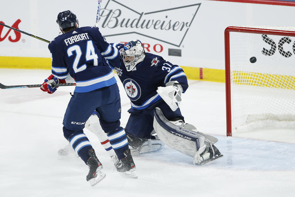 A deflection by Montreal Canadiens' Brendan Gallagher, not seen, goes off the crossbar behind Winnipeg Jets goaltender Connor Hellebuyck (37) as Derek Forbort (24) defends during the first period of an NHL hockey game Saturday, Feb. 27, 2021, in Winnipeg, Manitoba. (John Woods/The Canadian Press via AP)