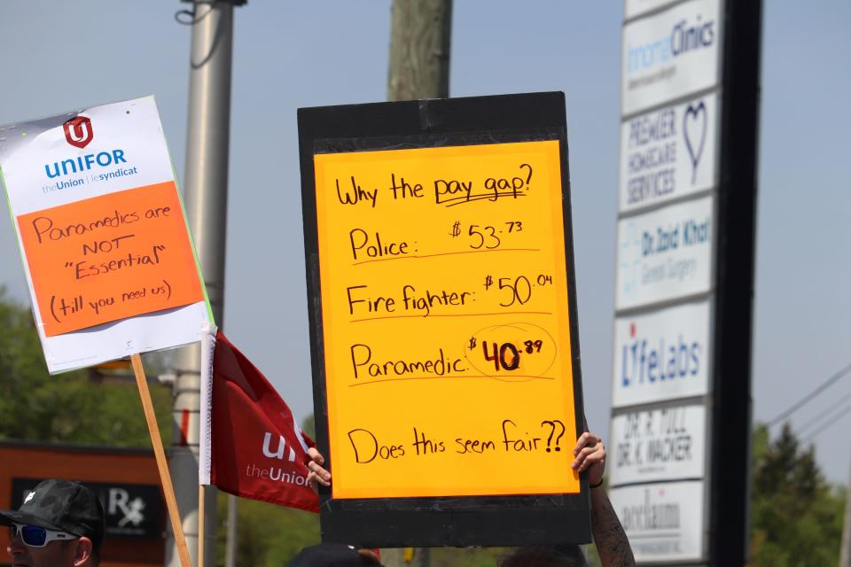 An attendee of Tuesday's Sault Ste. Marie paramedics rally holds up a sign that spells out the average hourly rate for a first-class Sault paramedic ($40.89), comparing that pay to an equivalent position in the local police department ($53.73) and fire service ($50.04)