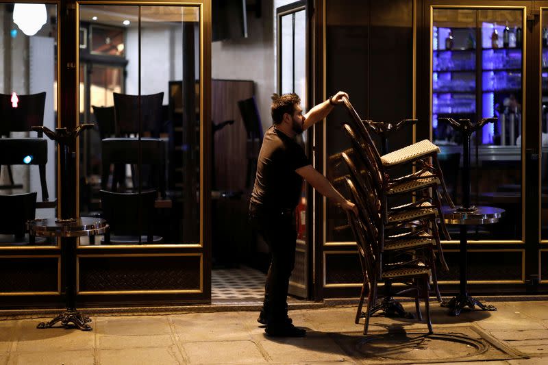 A bar employee clears out all the outside seats and prepares the closure of the place, as France's Prime Minister announced to close most all non-indispensable locations from midnight on Saturday, in Paris