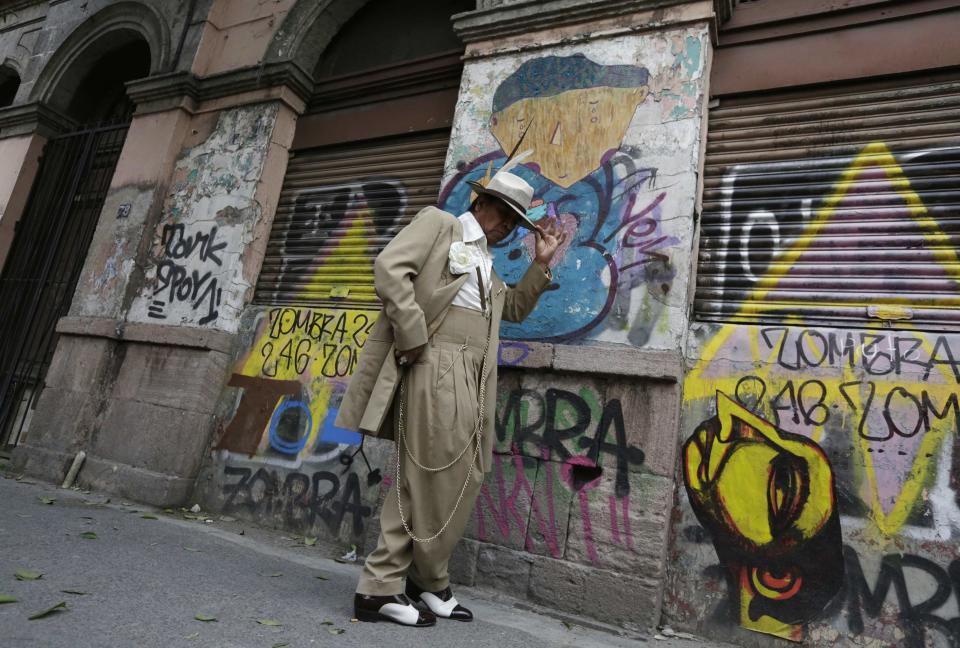 Ramirez wears his "Pachuco" outfit while posing for a photograph next to a wall with graffiti in Mexico City