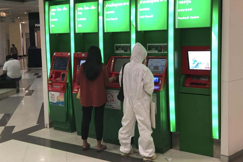 A person wearing full protective gear uses an ATM outside a bank Bangkok, Thailand, Wednesday, July 21, 2021. (AP Photo/Grant Peck)