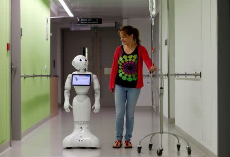 A woman walks with new recruit "Pepper" the robot, a humanoid robot designed to welcome and take care of visitors and patients, at AZ Damiaan hospital in Ostend, Belgium June 16, 2016. REUTERS/Francois Lenoir