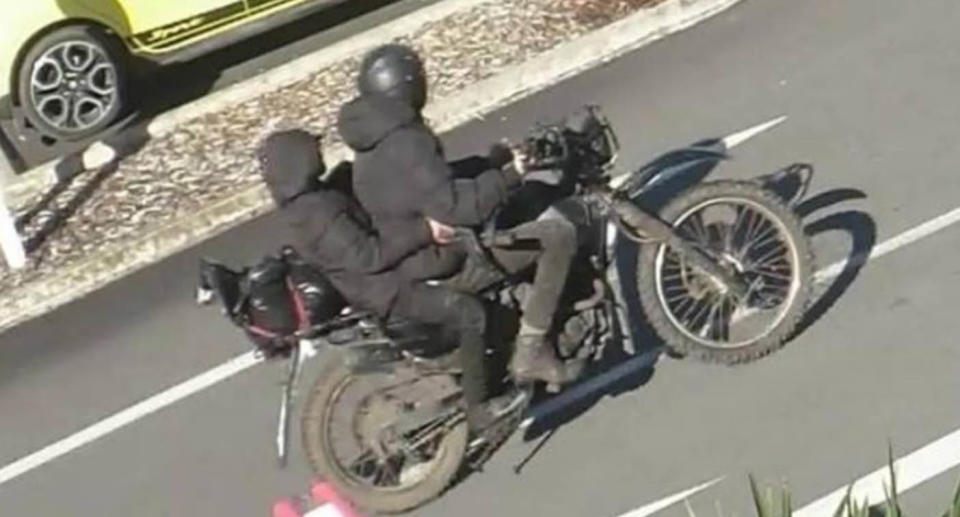 Two people wearing black on back of motorbike. 