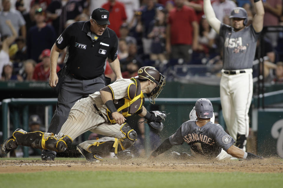 Washington Nationals' César Hernández (1) slides into home plate on a hit by single by Victor Robles as San Diego Padres catcher Austin Nola, front left, attempts a tag during the seventh inning of a baseball game, Saturday, Aug. 13, 2022, in Washington. A replay review showed that Nola blocked the plate and the score counted. (AP Photo/Luis M. Alvarez)