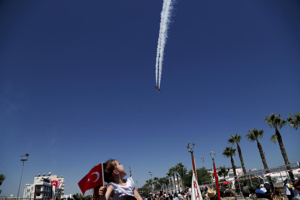 A girl sits on her father's shoulders as they watch the Turkish acrobatic aircraft jets perform, during a military parade celebration marking the 45th anniversary of the 1974 Turkish invasion in the Turkish occupied area of the divided capital Nicosia, Cyprus, Saturday, July 20, 2019. Cyprus was split into Greek Cypriot south and Turkish Cypriot north in 1974 when Turkey invaded in response to a coup by supporters of union with Greece. (AP Photo/Petros Karadjias)