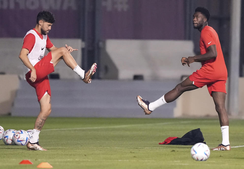 Canada forward Alphonso Davies, right, stretches his leg next to teammate Jonathan Osorio during practice at the World Cup in Doha, Qatar, on Monday, Nov. 21, 2022. (Nathan Denette/The Canadian Press via AP)