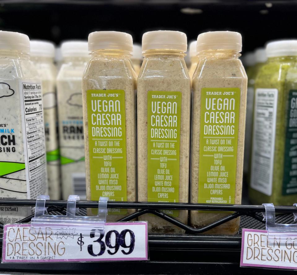 Three bottles of Trader Joe's vegan Ceasar dressing on a shelf at Trader Joe's. The bottles have green labels