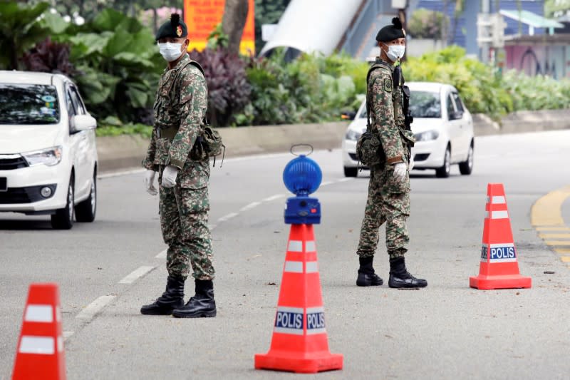 Soldiers wearing protective masks stand guard at a roadblock in Kuala Lumpur