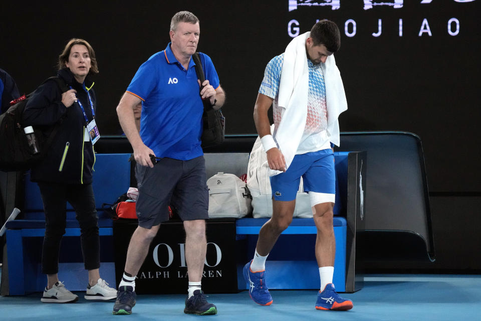 Novak Djokovic, right, of Serbia leaves the court with a trainer for an injury time out during his second round match against Enzo Couacaud of France at the Australian Open tennis championship in Melbourne, Australia, Thursday, Jan. 19, 2023. (AP Photo/Dita Alangkara)