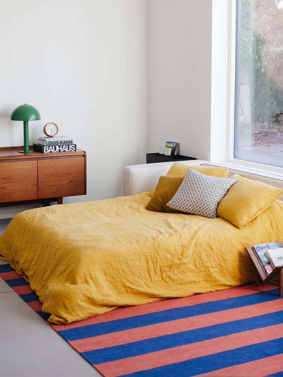 Bed with yellow bedspread and striped rug.