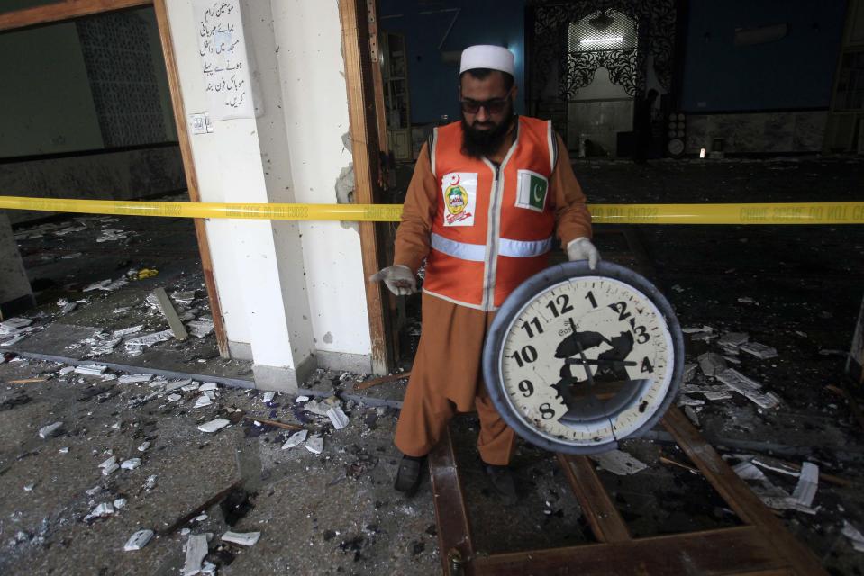 Rescue worker holds a damaged wall clock as he stands amidst the debris after an explosion in a Shi'ite mosque in Peshawar