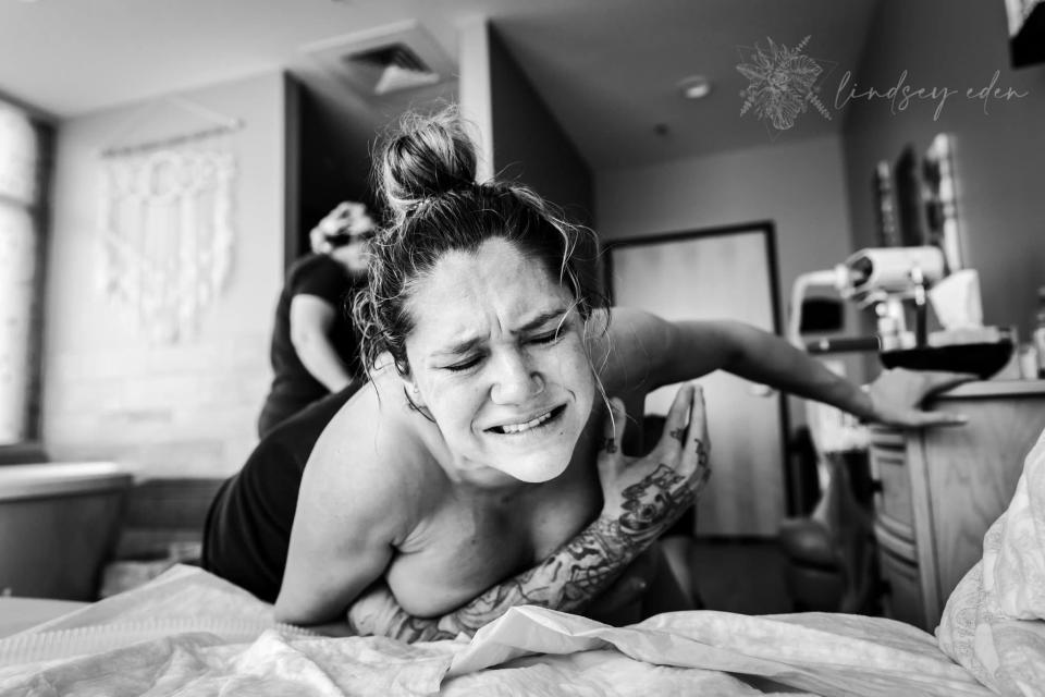 A wincing woman leans over a bed in laborA