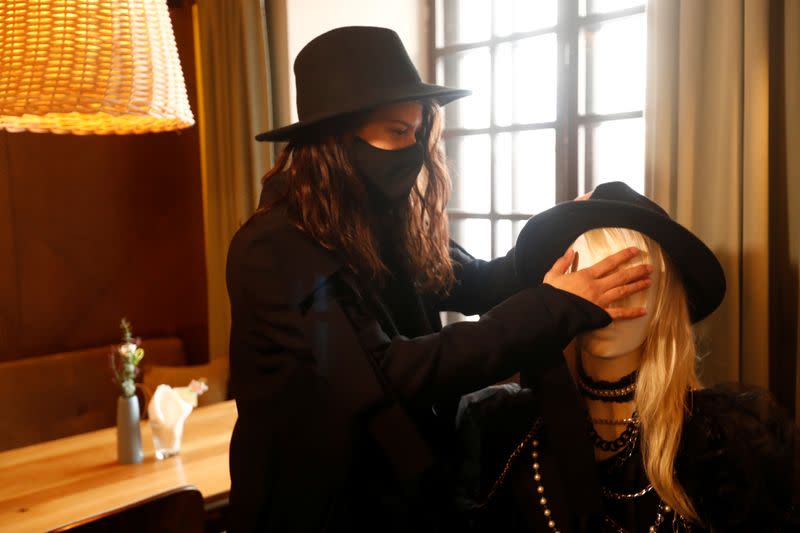 A woman wearing a protective face mask interacts with a mannequin dressed in creations of local designer as it sits at the table in a restaurant, during the coronavirus disease (COVID-19) outbreak in Vilnius