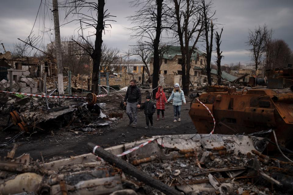 A family walks amid destroyed Russian tanks in Bucha, on the outskirts of Kyiv, Ukraine, Wednesday, April 6, 2022 (Copyright 2022 The Associated Press. All rights reserved.)