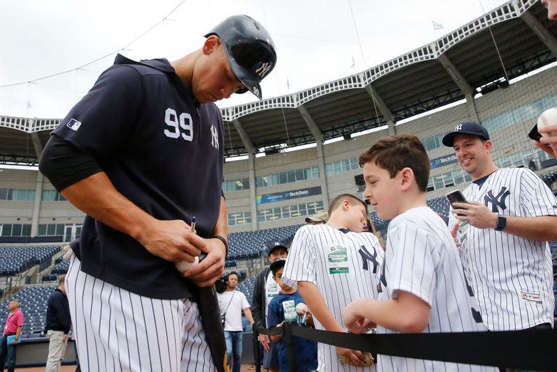 Aaron Judge #99 of the New York Yankees signs a autograph for a fan prior to the Grapefruit League spring training game against the Philadelphia Phillies at Steinbrenner Field on February 26, 2019 in Tampa, Florida.