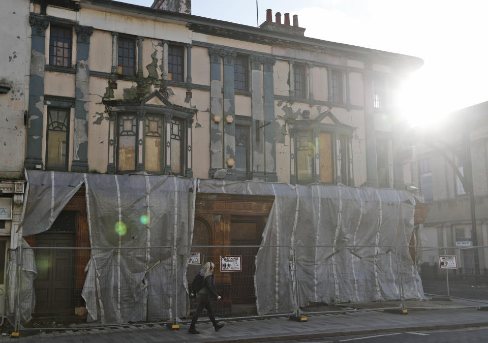 A woman walks past a dilapidated former public house boarded up on the high street in Hartlepool, England, Monday, Nov. 11, 2019. Political parties in Britain's Brexit-dominated December election are battling fiercely to win Hartlepool and places like it: working-class former industrial towns with voters who could hold the key to the prime minister's office at 10 Downing Street. Hartlepool, a former shipbuilding center 250 miles (400 kms) north of London where unemployment is more than double the national average, is a town full of leavers. (AP Photo/Frank Augstein)