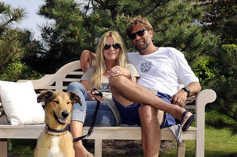 Klopp in shorts, Ulla in denim, sitting on a bench with a tan coloured dog in front