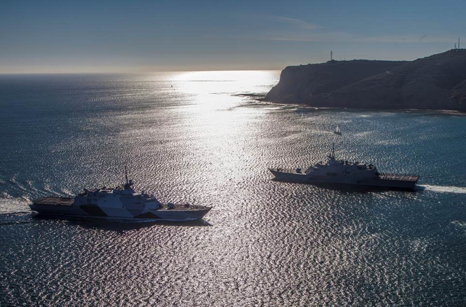 Two Lockheed Martin Freedom-class LCS two ship on maneuvers as the sun sets behind them.