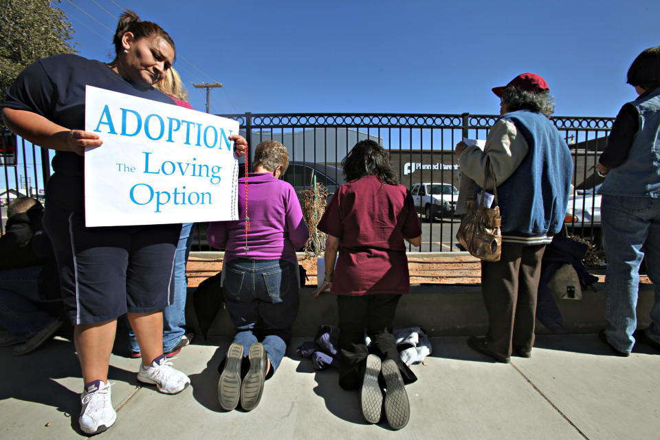 FILE - In this Friday, Jan. 20, 2012 file photo, Norma Castillo, left, holds a sign as other anti-abortion demonstrators kneel and pray facing the Midland Planned Parenthood clinic to mark the 39th anniversary of Roe vs. Wade in Midland, Texas. Planned Parenthood, which closed abortion clinics in Lubbock and Midland in 2013, hopes to re-establish its presence in the region. (Heather Leiphart/Odessa American via AP)