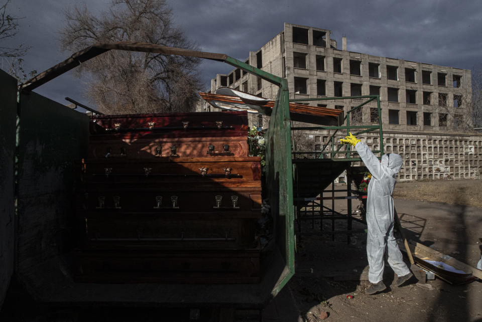 A cemetery worker places used coffins into a receptacle to be collected and destroyed by a contractor, at La Recoleta cemetery in Santiago, Chile, Wednesday, April 21, 2021, amid the new coronavirus pandemic. (AP Photo/Esteban Felix)