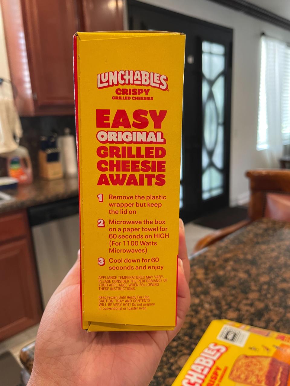 A hand holding a Lunchables Grilled Cheese box with instructions on how to prepare the meal