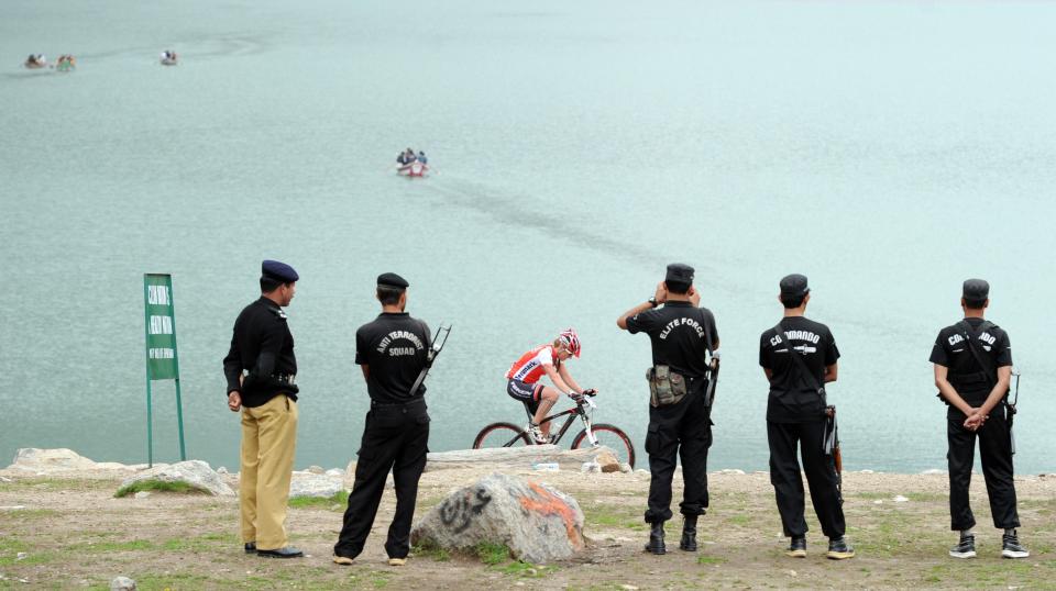 Pakistani policemen stand guard as an international cyclist competes during the second stage of the Himalayas 2011 International Mountainbike Race in the mountainous area of Lake Saif-ul-Maluk in Pakistan's tourist region of Naran in Khyber Pakhtunkhwa province on September 17, 2011. The cycling event, organised by the Kaghan Memorial Trust to raise funds for its charity school set up in the Kaghan valley for children affected in the October 2005 earthquake, attracted some 30 International and 11 Pakistani cyclists. AFP PHOTO / AAMIR QURESHI (Photo credit should read AAMIR QURESHI/AFP/Getty Images)
