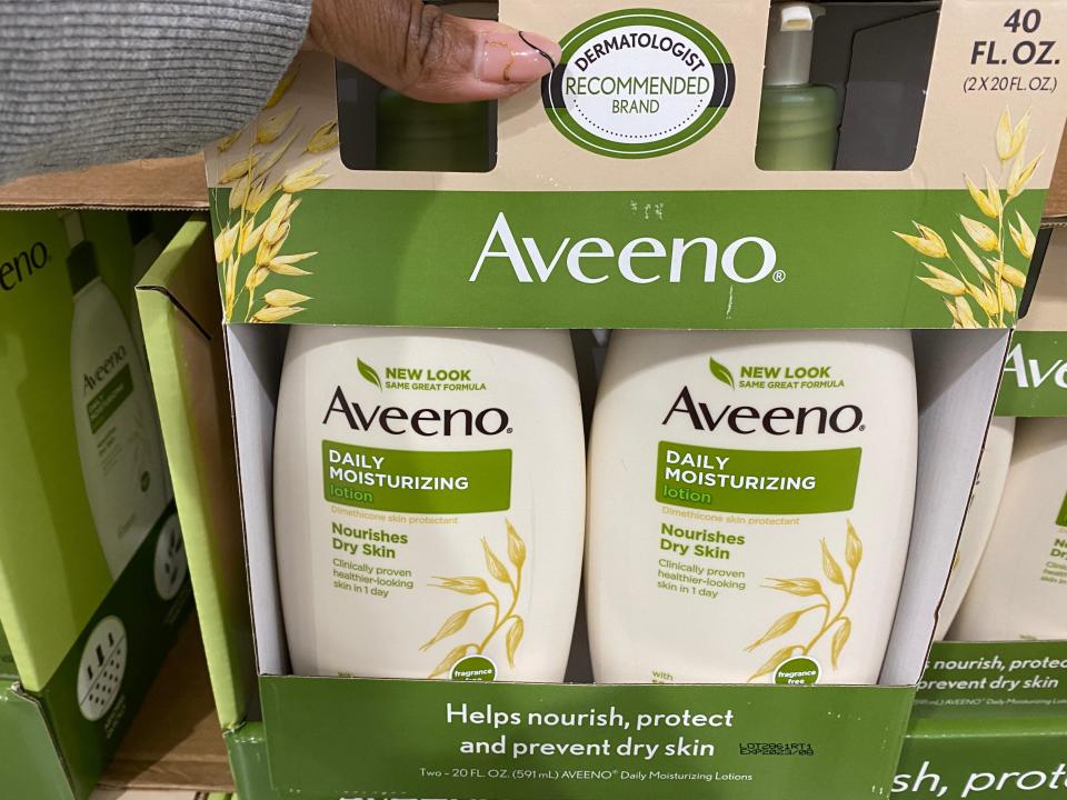 The writer holds a two-pack of Aveeno moisturizer with white and green packaging