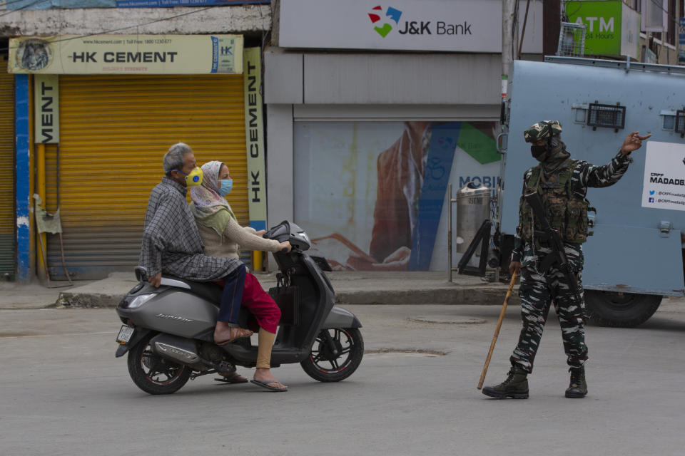 FILE- In this April 7, 2020 file photo, an Indian paramilitary soldier stops people on a scooter during lockdown in Srinagar, Indian controlled Kashmir. India, a bustling country of 1.3 billion people, has slowed to an uncharacteristic crawl, transforming ordinary scenes of daily life into a surreal landscape. The country is now under what has been described as the world’s biggest lockdown, aimed at keeping the coronavirus from spreading and overwhelming the country’s enfeebled health care system. (AP Photo/ Dar Yasin, File)