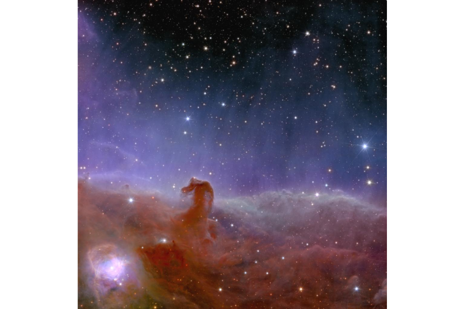 At the bottom of the screen, lots of hazy-looking reddish gas comes together to form a small hook shape to the left.  Above is a purple glow that fades towards the top of the image, indicating a dark region of space with starry dots.