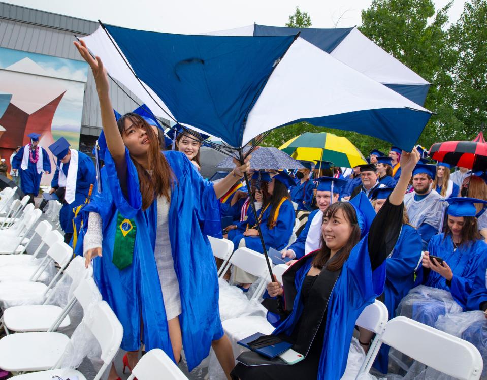 International students Kewalin Inta, left, and Waka Nishimura, struggle with their umbrella during a downpour at the 2022 Lane Community College graduation Saturday.