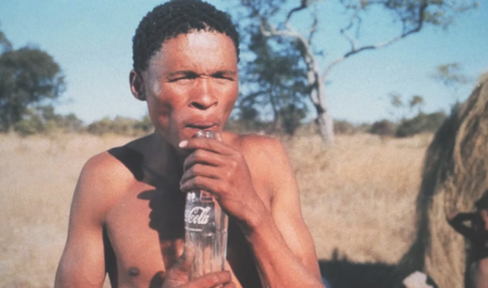 A shirtless N!xau in Africa holding the coke bottle that fell from the sky