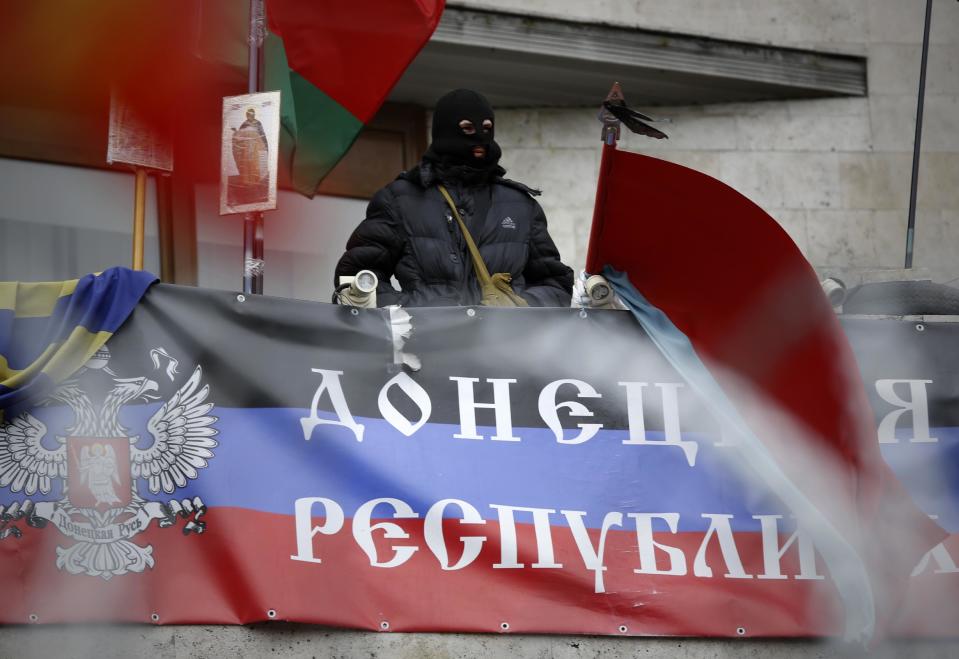 A masked pro-Russian activist looks from a balcony of the regional administration building decorated with a banner reading "Donetsk Republic" in Donetsk, Ukraine, Saturday, April 12, 2014. The unrest in Donetsk and Slovyansk, about 90 kilometers (55 miles) to the north, were the latest shows of spiraling anger in eastern Ukraine, which has a large Russian-speaking population and was also the support base for Viktor Yanukovych, the Ukrainian president who was ousted in February after months of protests in the capital, Kiev.(AP Photo/Max Vetrov)