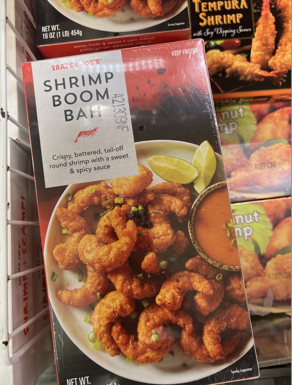 Trader Joe's Shrimp Boom Bah! package on a freezer shelf. It shows crispy, battered shrimp with slices of lime and a dipping sauce on the side