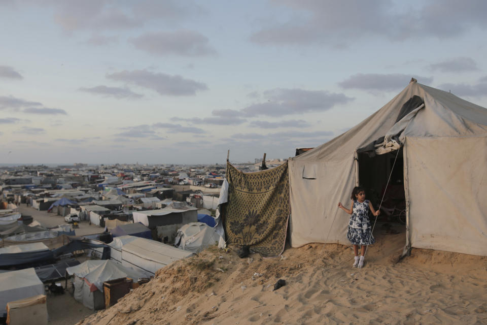 A Palestinian girl stands at the entrance of her family tent at a makeshift tent camp for those displaced by the Israeli air and ground offensive on the Gaza Strip in Khan Younis, Gaza, Tuesday, June 18, 2024. (AP Photo/Jehad Alshrafi)