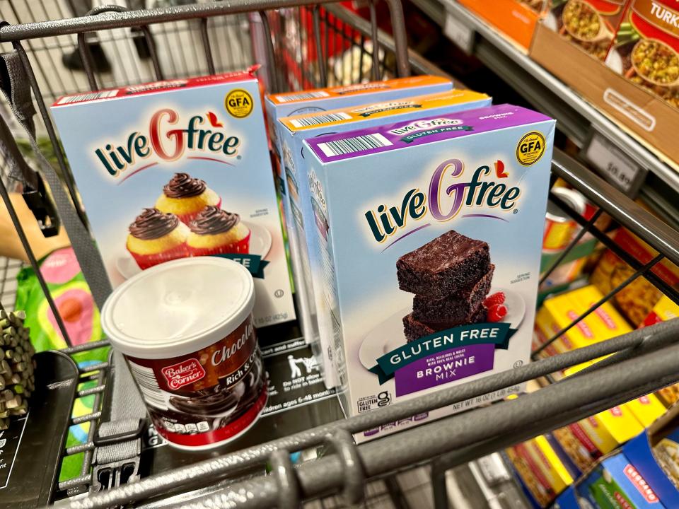 Live G Free brownie and cake mixes in a cart with Baker's Corner chocolate frosting can. The can of frosting has a black label and the boxes of the mixes are blue