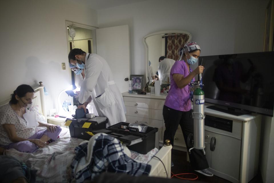 Doctor Leonardo Acosta and nurse Marlene Cabezas, center left, care for Carmen Lares, left, who suffers from COVID-19 along with her husband, as assistant Jane Caro, right, brings in an oxygen tank, at their home in Caracas, Venezuela, Thursday, March 18, 2021. The Lares family is being treated at home for the last 4 days. (AP Photo/Ariana Cubillos)