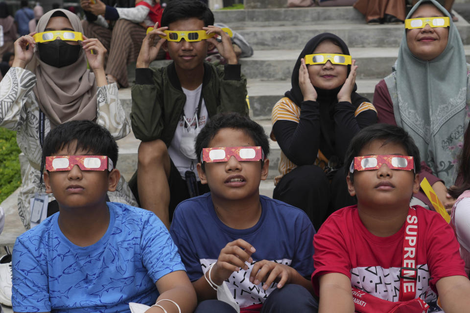 Children wear protective glasses and appear to be looking up in the same direction.