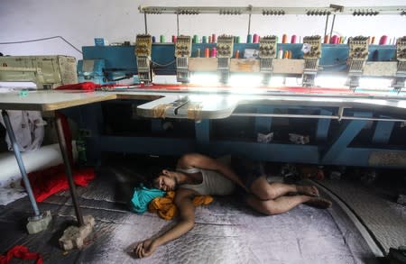 A worker sleeps underneath an embroidery machine at a workshop in Mumbai